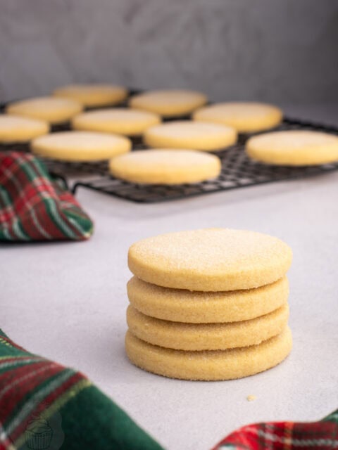 Stack of round Scottish Shortbread biscuits beside more biscuits on a wire cooling rack.