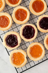 Freshly baked jam tarts with raspberry and apricot filling cooling on a wire rack