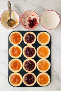 Jam tarts in a baking tray filled with apricot and raspberry jam before baking