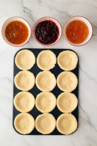 Unbaked shortcrust pastry cases pressed into a tart tray ready for jam filling