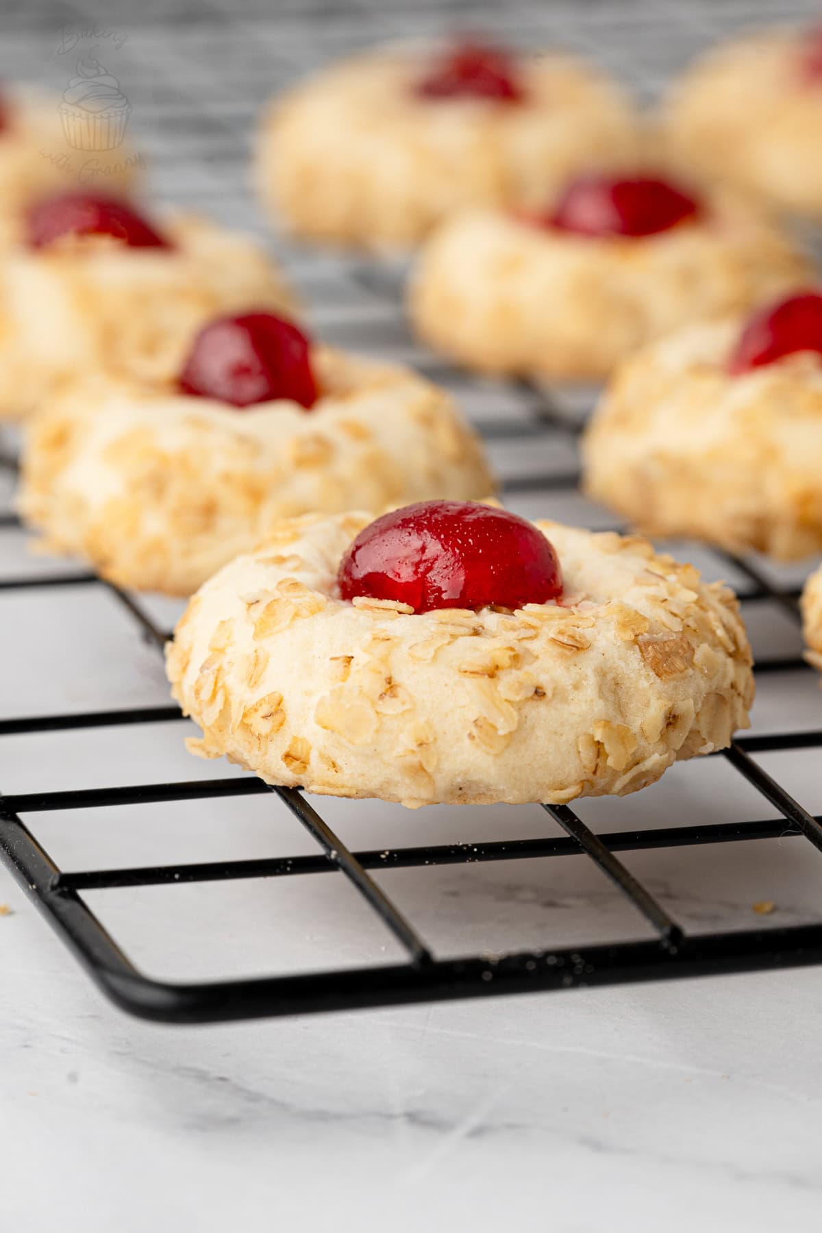 Oat-coated Melting Moment topped with half a glacé cherry on a cooling rack.