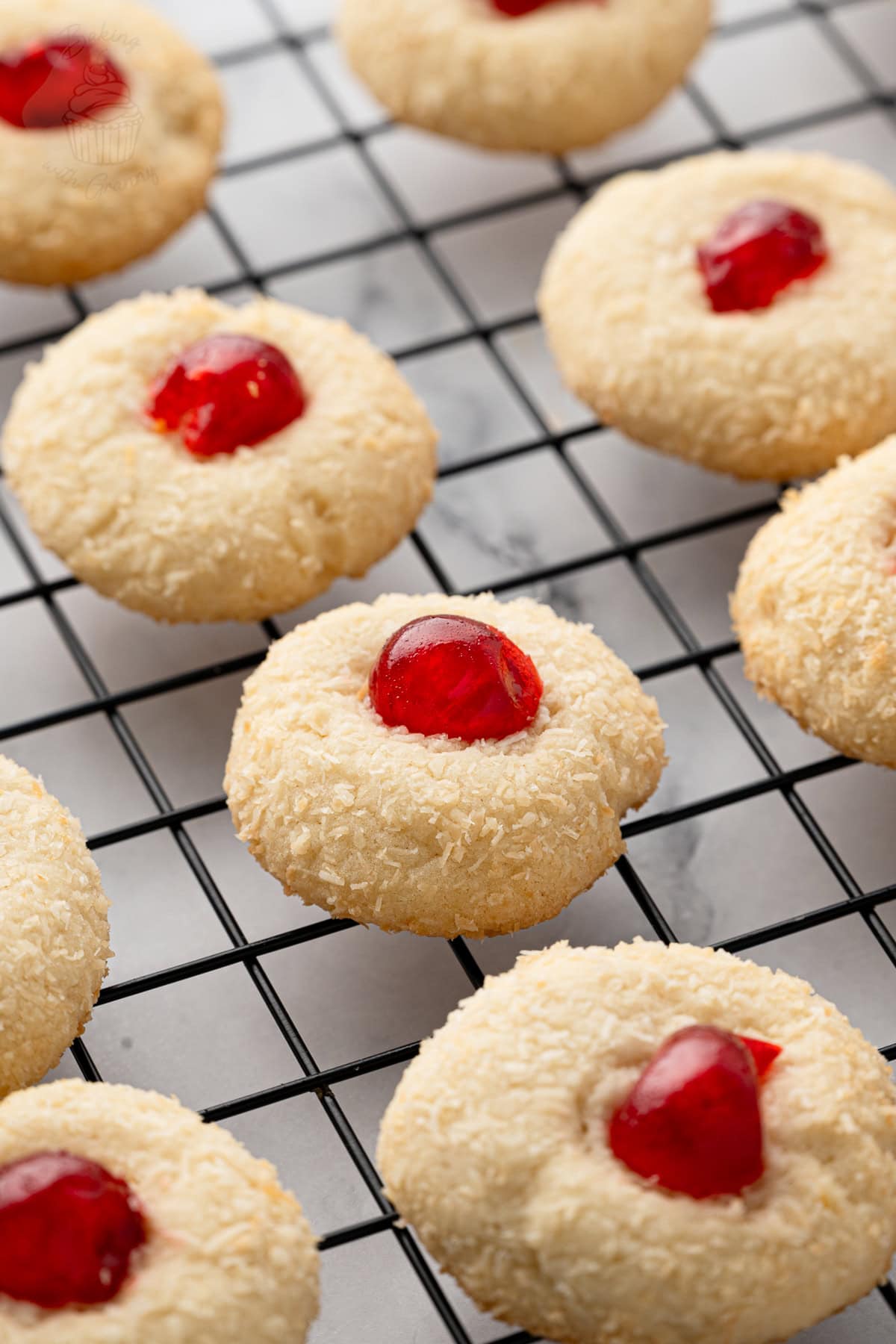Coconut-coated Melting Moments topped with glacé cherries on a wire cooling rack.
