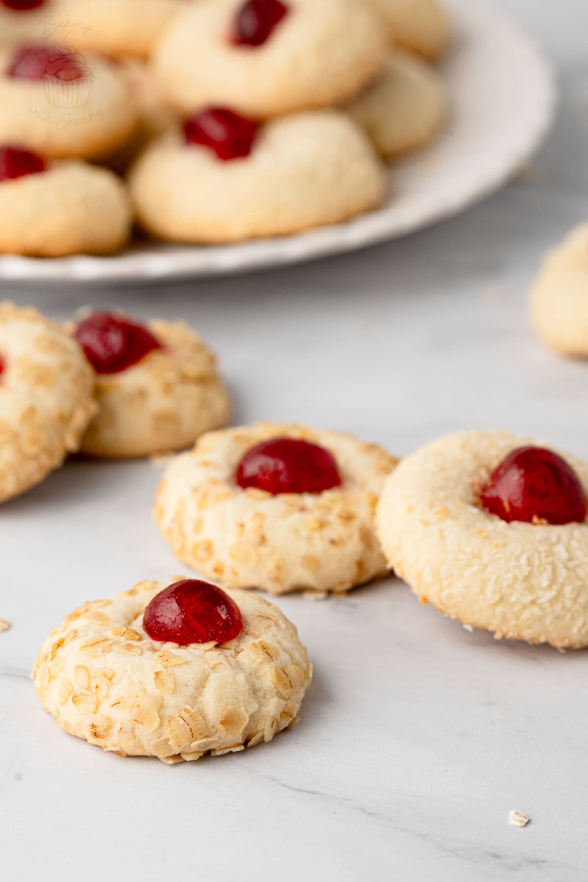 Oat and coconut-coated Melting Moments topped with glacé cherries on a table.