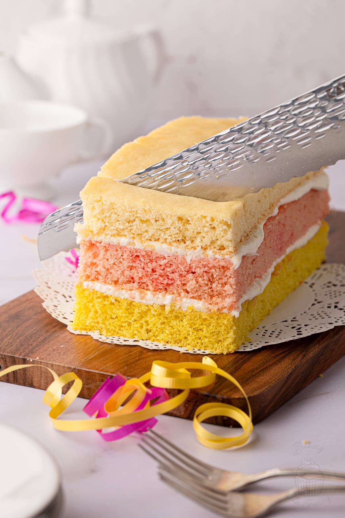 British Angel Cake being sliced to reveal its colourful sponge layers and buttercream filling.
