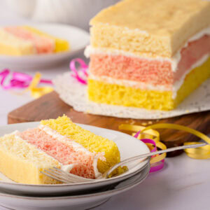 Traditional British Angel Cake on a wooden board with a slice served in the background.