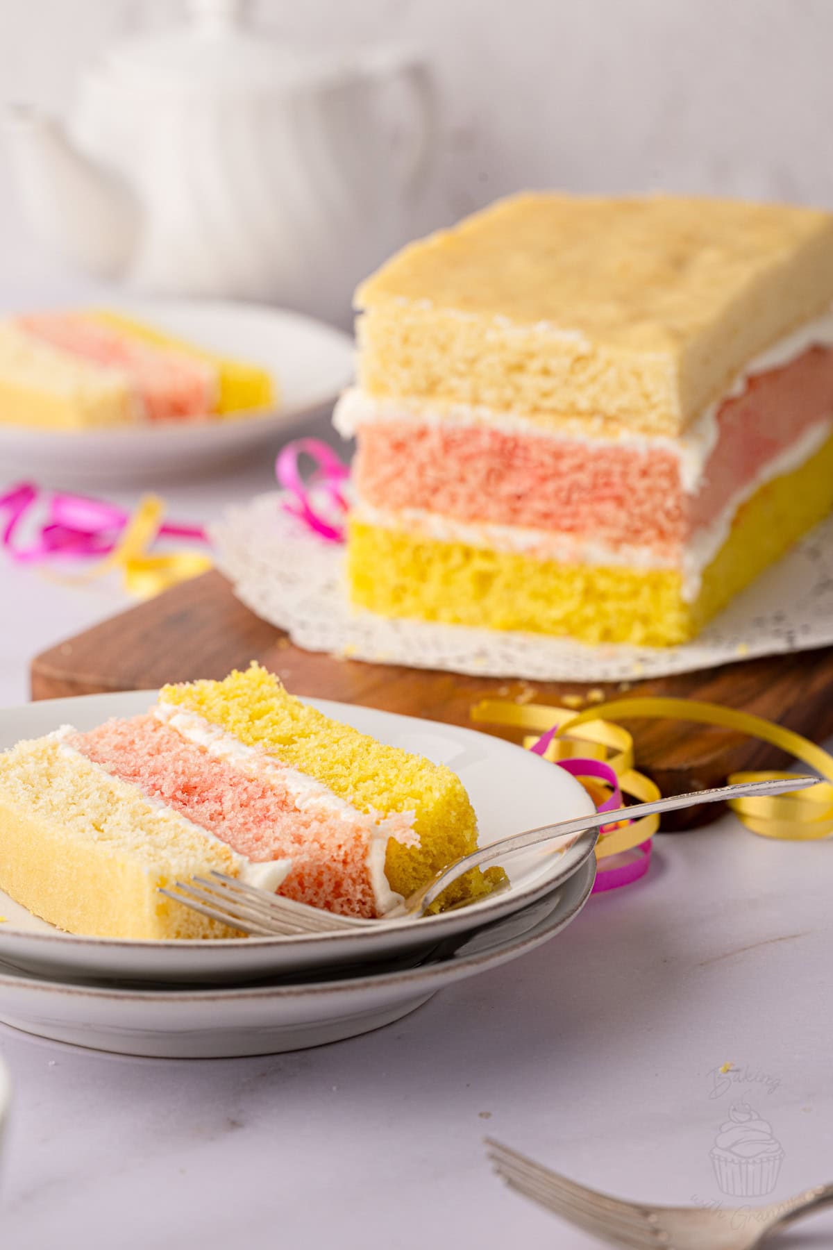 Traditional British Angel Cake on a wooden board with a slice served in the background.