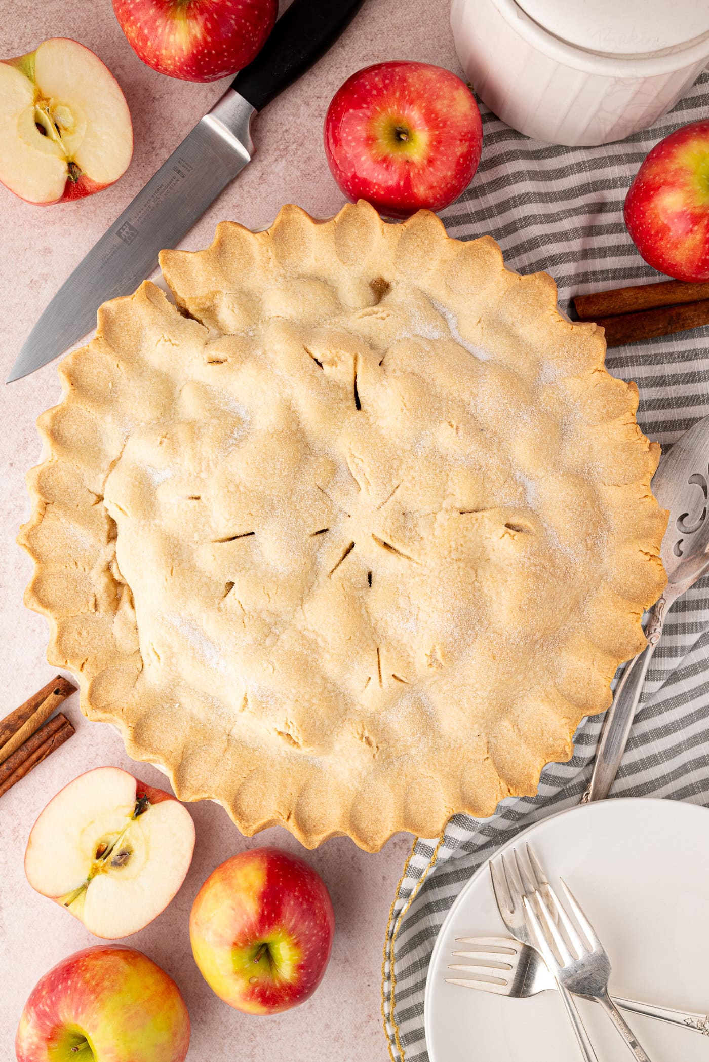 Apple Pie Top-down photo of a baked apple pie, styled with apples, cinnamon sticks, and cutlery. A seasonal apple pie UK recipe with classic flavours.