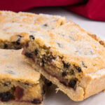 Close-up of a sliced Paradise Slice with a crumbly golden top, currants, cherries, and jam filling.