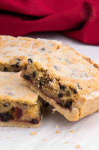 Close-up of a sliced Paradise Slice with a crumbly golden top, currants, cherries, and jam filling.