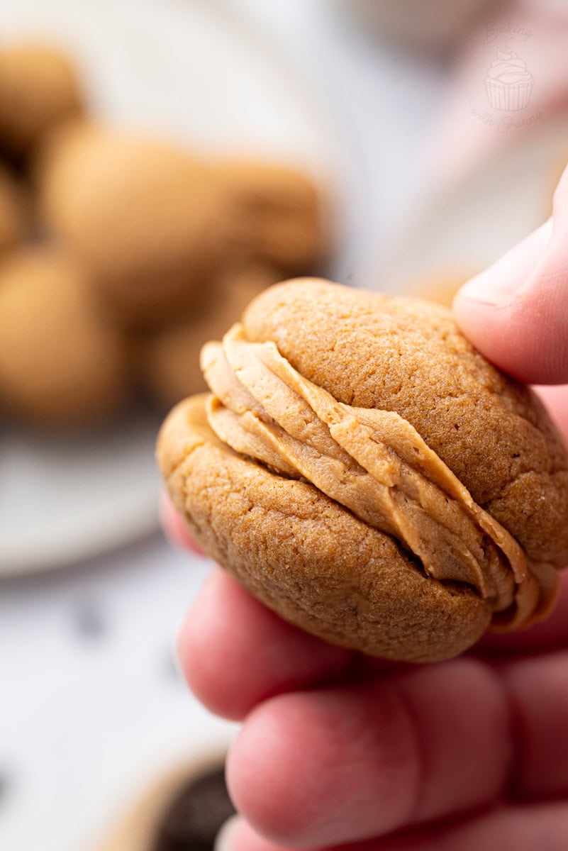 Hand holding a coffee kisses cookie filled with coffee buttercream.