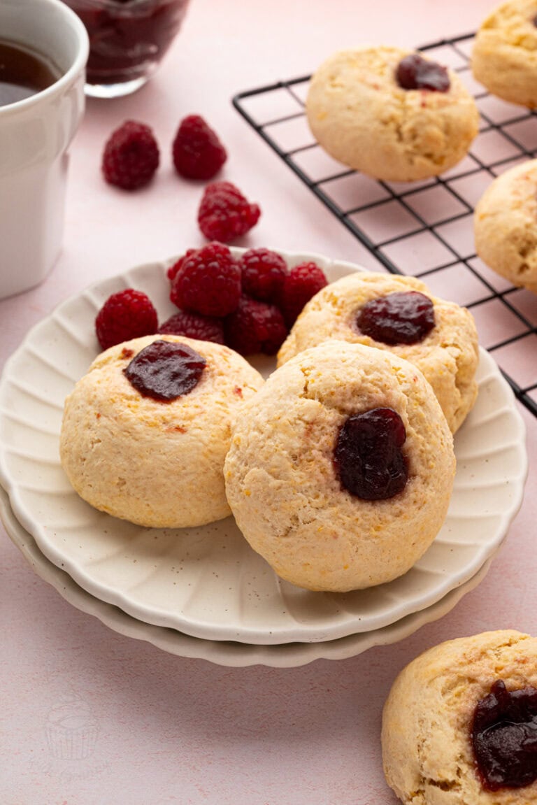 Three raspberry jam buns stacked on a plate with fresh raspberries and tea in the background.