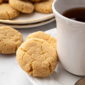Gingernut biscuit resting against a teacup on a saucer.