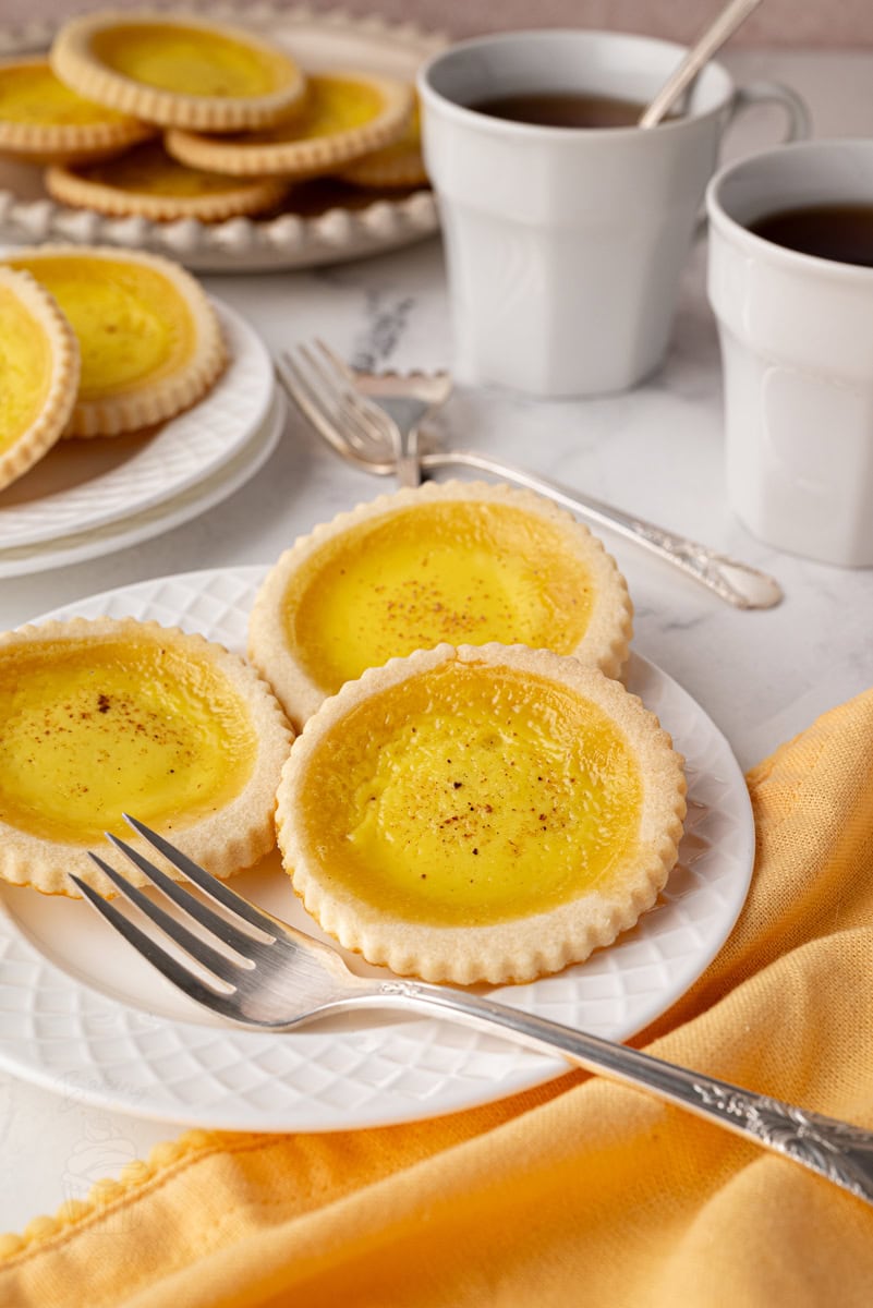 Overhead shot of three custard tarts with warm yellow custard and sweet shortcrust pastry, placed near vintage forks.
