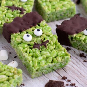 Green Frankenstein Rice Krispies Square with chocolate hair, edible eyes and a chocolate mouth with more squares behind.