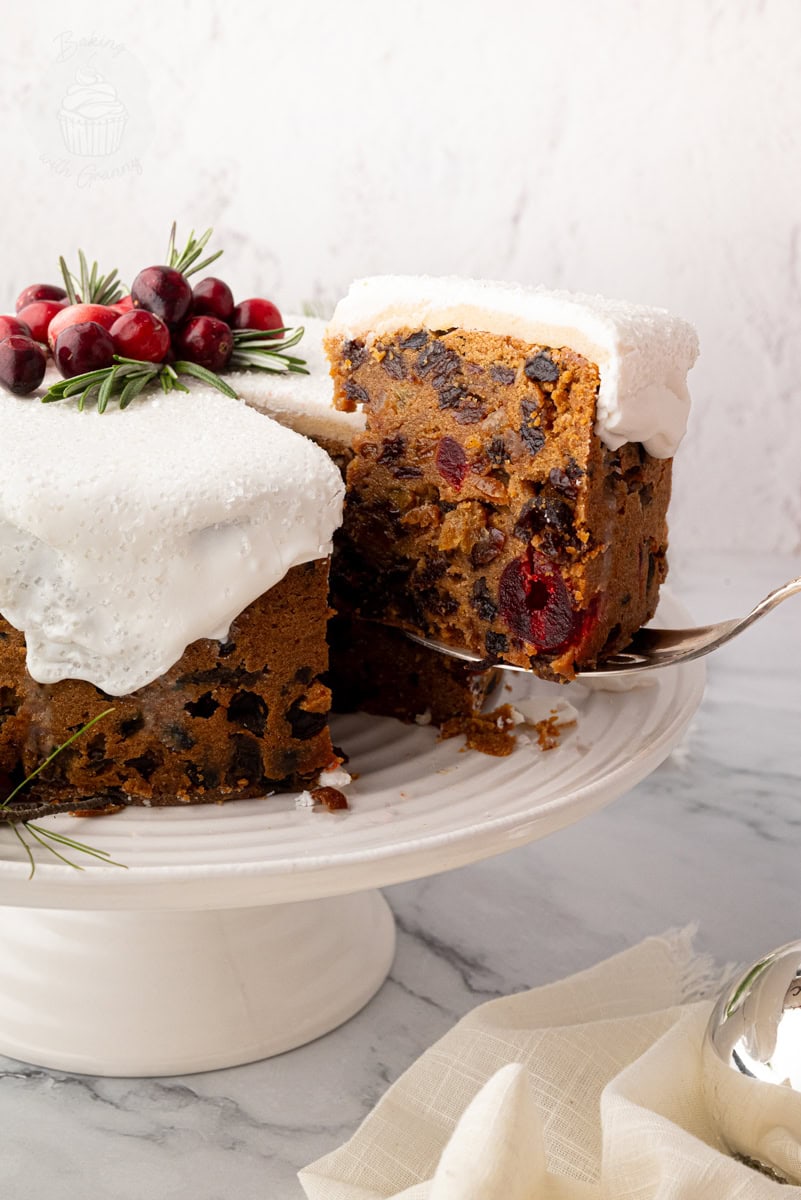 Classic British Christmas cake with a slice being lifted from the cake stand, showing dense fruit cake texture. Traditional UK Christmas cake recipe.