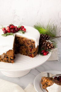 Iced Christmas cake with a wedge removed, revealing dried fruit and cherries inside.