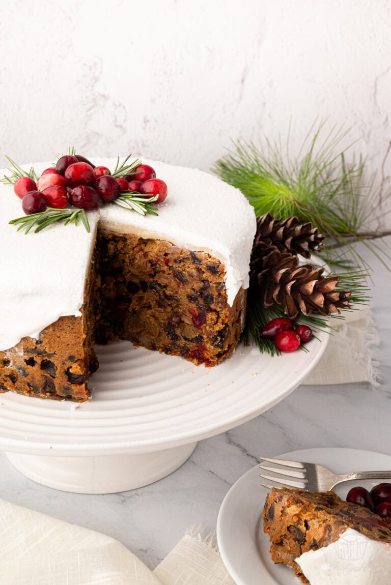 Iced Christmas cake with a wedge removed, revealing dried fruit and cherries inside.