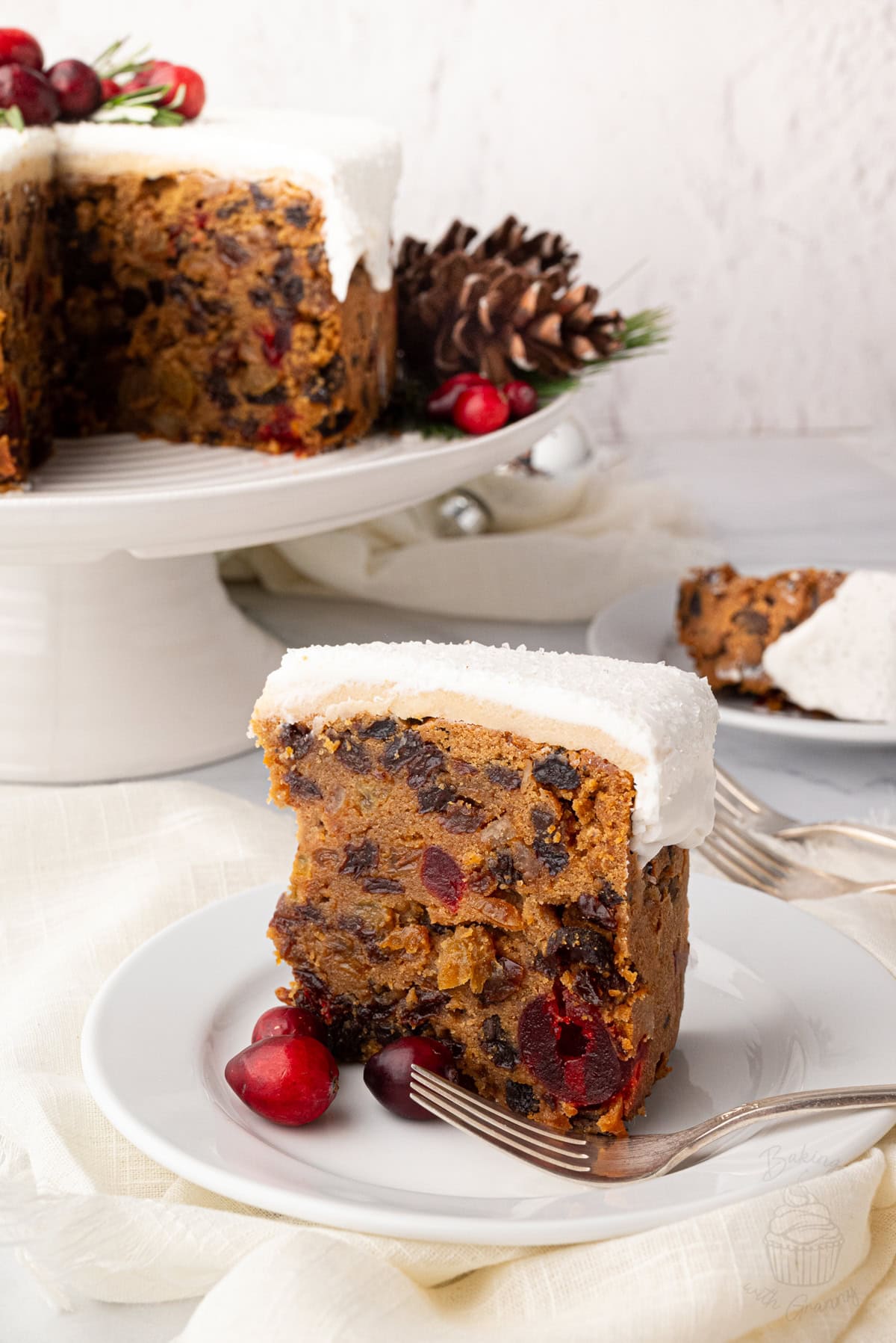 A slice of Christmas cake with white icing, served with cranberries on a plate.