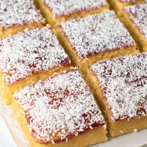 Close-up of a slice of old school cake on baking paper, with golden sponge, vibrant jam, and coconut.