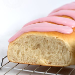 Close up of an Iced Finger Bun. Soft doughy bun, topped with sticky pink icing.