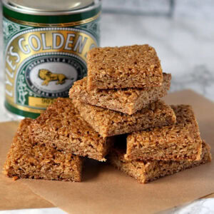 Stack of golden-brown flapjack squares beside a tin of Lyle’s Golden Syrup