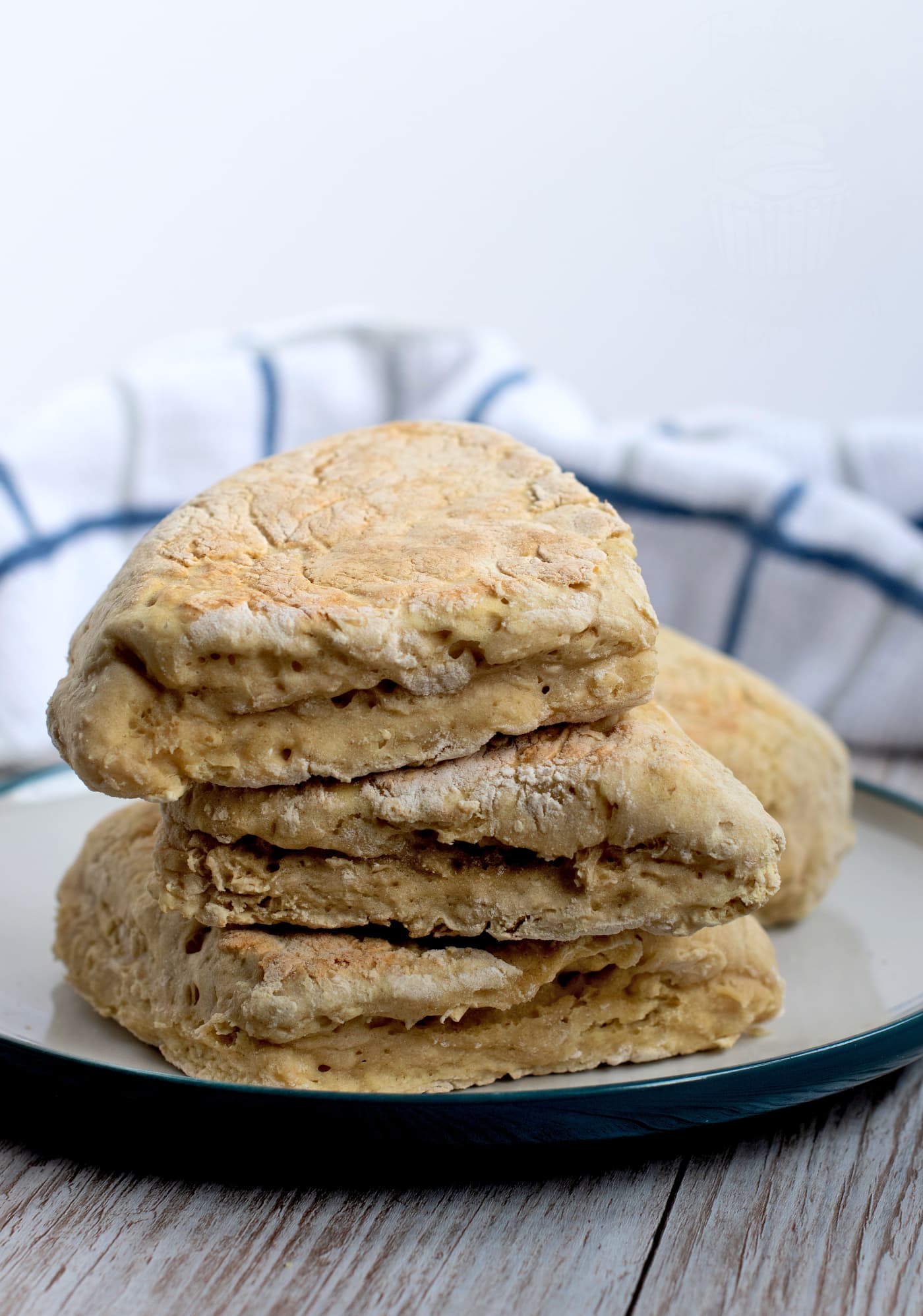 A stack of four triangular soda farls, akin to the best Irish recipe, sits on a plate with a blue rim. The soda farls boast a golden-brown exterior. A white cloth with blue stripes is blurred in the background.