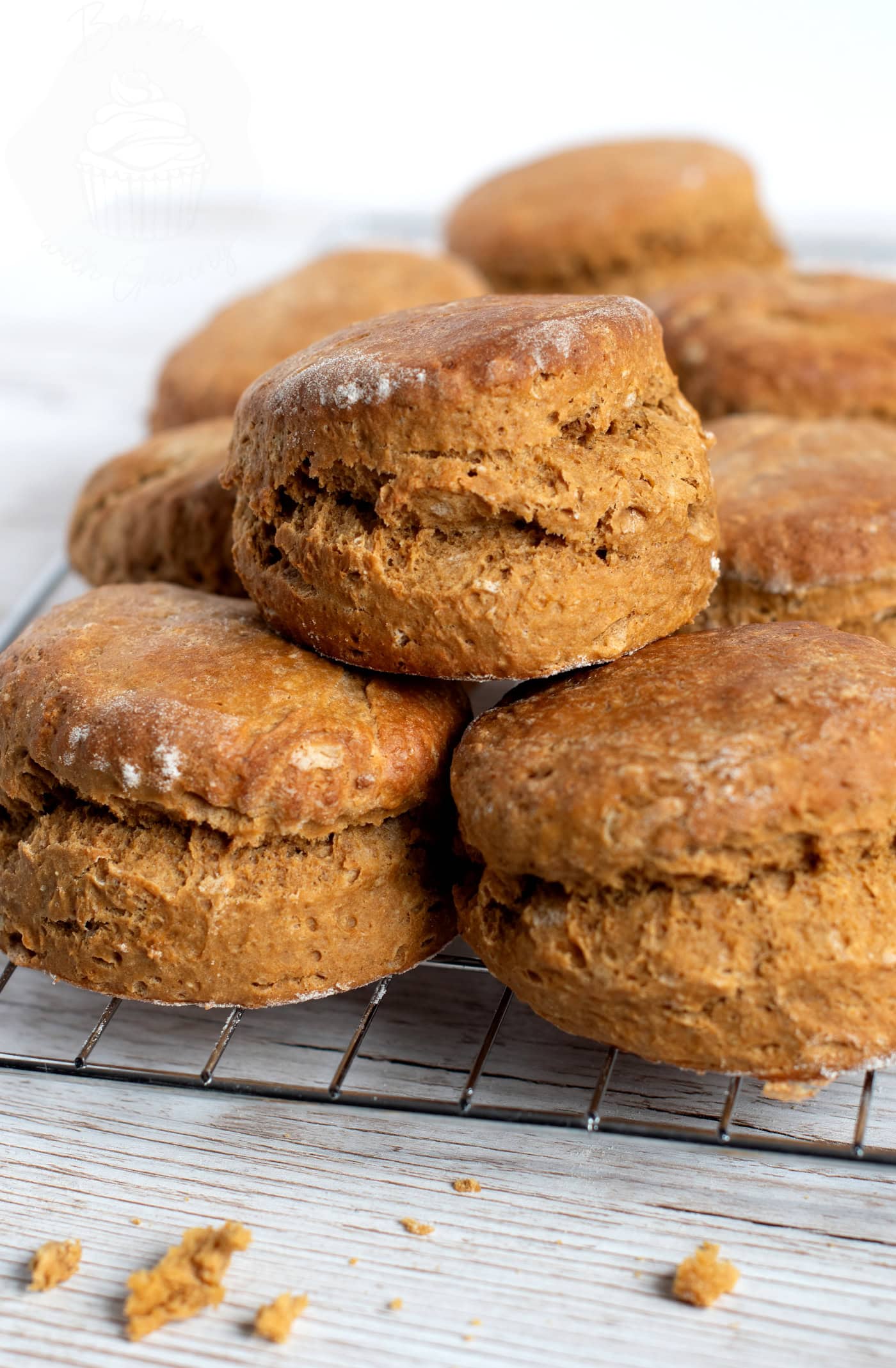 Freshly baked Scottish treacle scones stacked on a wire rack with a light wooden background. Some crumbs are scattered around the scones, highlighting their rich texture.