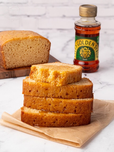 Stack of syrup-drizzled golden syrup cake slices with a bottle of golden syrup in the background.