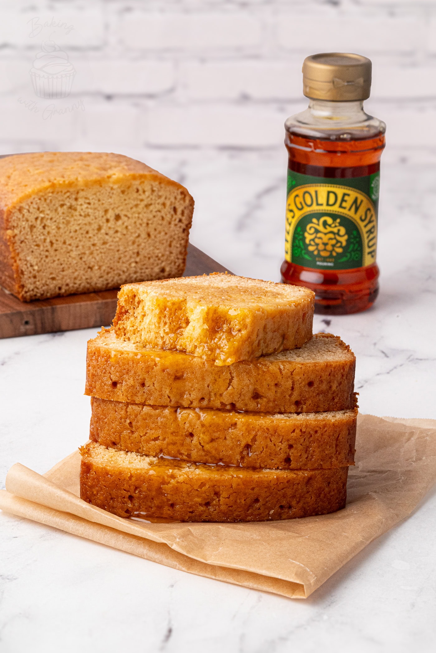 Stack of syrup-drizzled golden syrup cake slices with a bottle of golden syrup in the background.