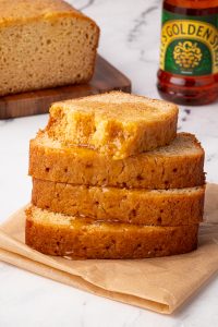 Close-up of golden syrup cake stack with syrup bottle and loaf in the background.