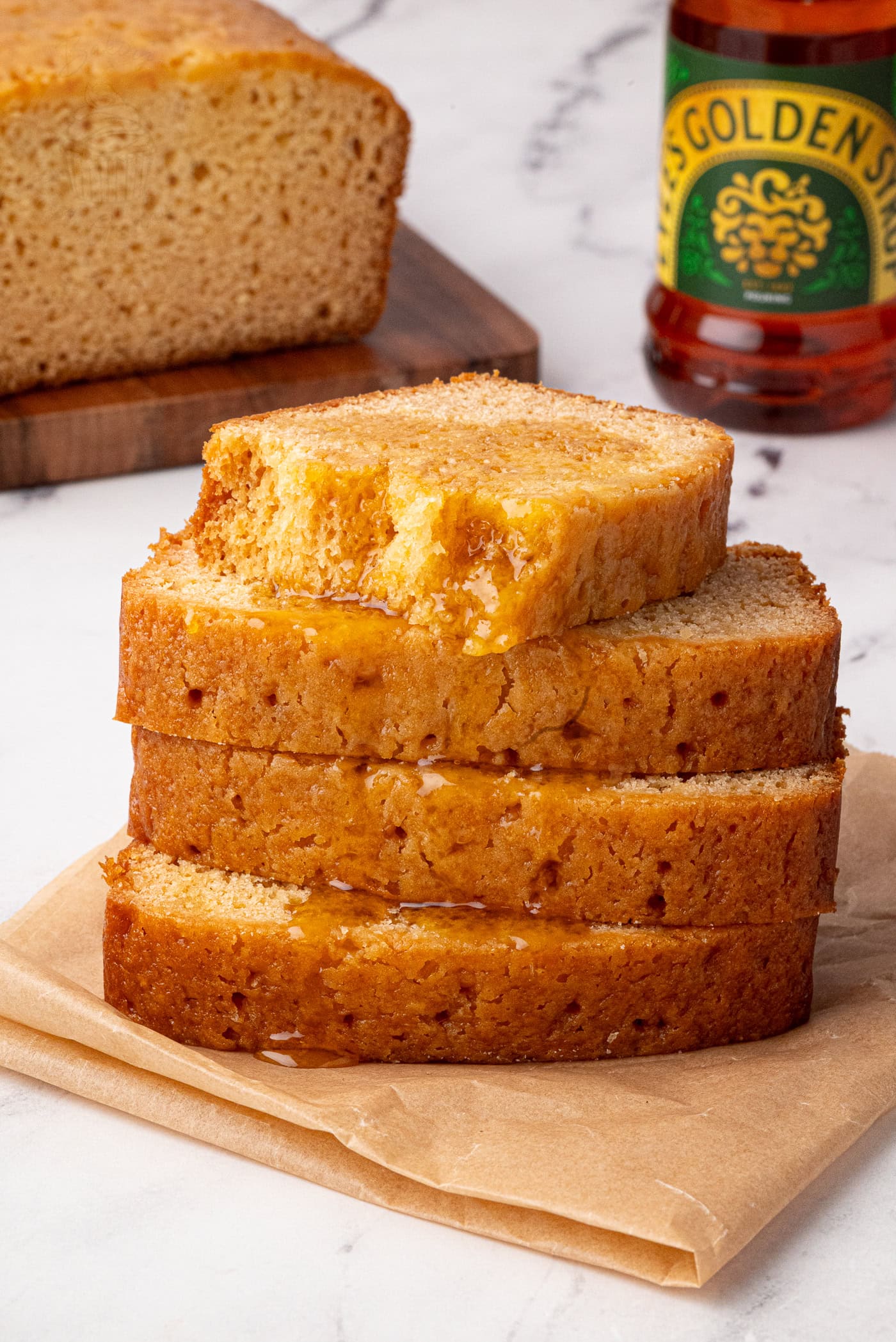 Close-up of golden syrup cake stack with syrup bottle and loaf in the background.