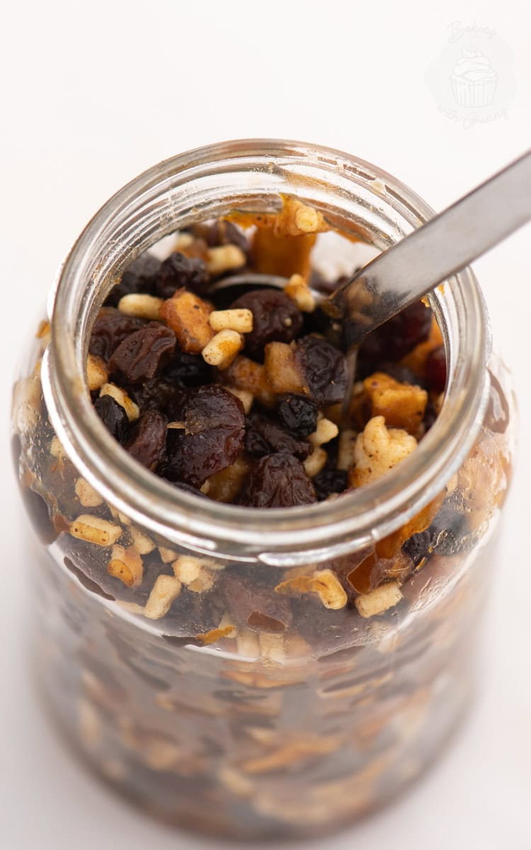 Top-down view into a jar of homemade Christmas mincemeat with raisins, apple, and mixed peel, and a spoon resting inside.