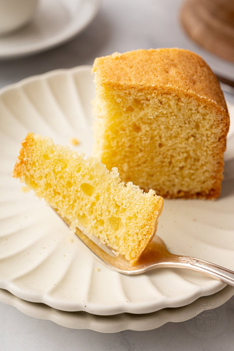 Slice of traditional Madeira cake lifted from the whole cake on a wooden cake stand.