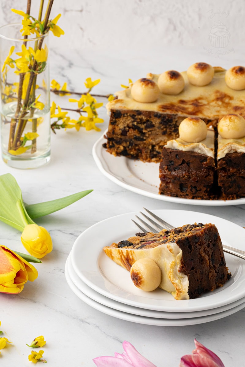 Simnel Cake slice plated with fork and tea, styled with colourful tulips on a light background.