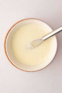 Bowl of whisked egg yolk, milk, sugar and custard powder mixture for making traditional Manchester Tart filling.