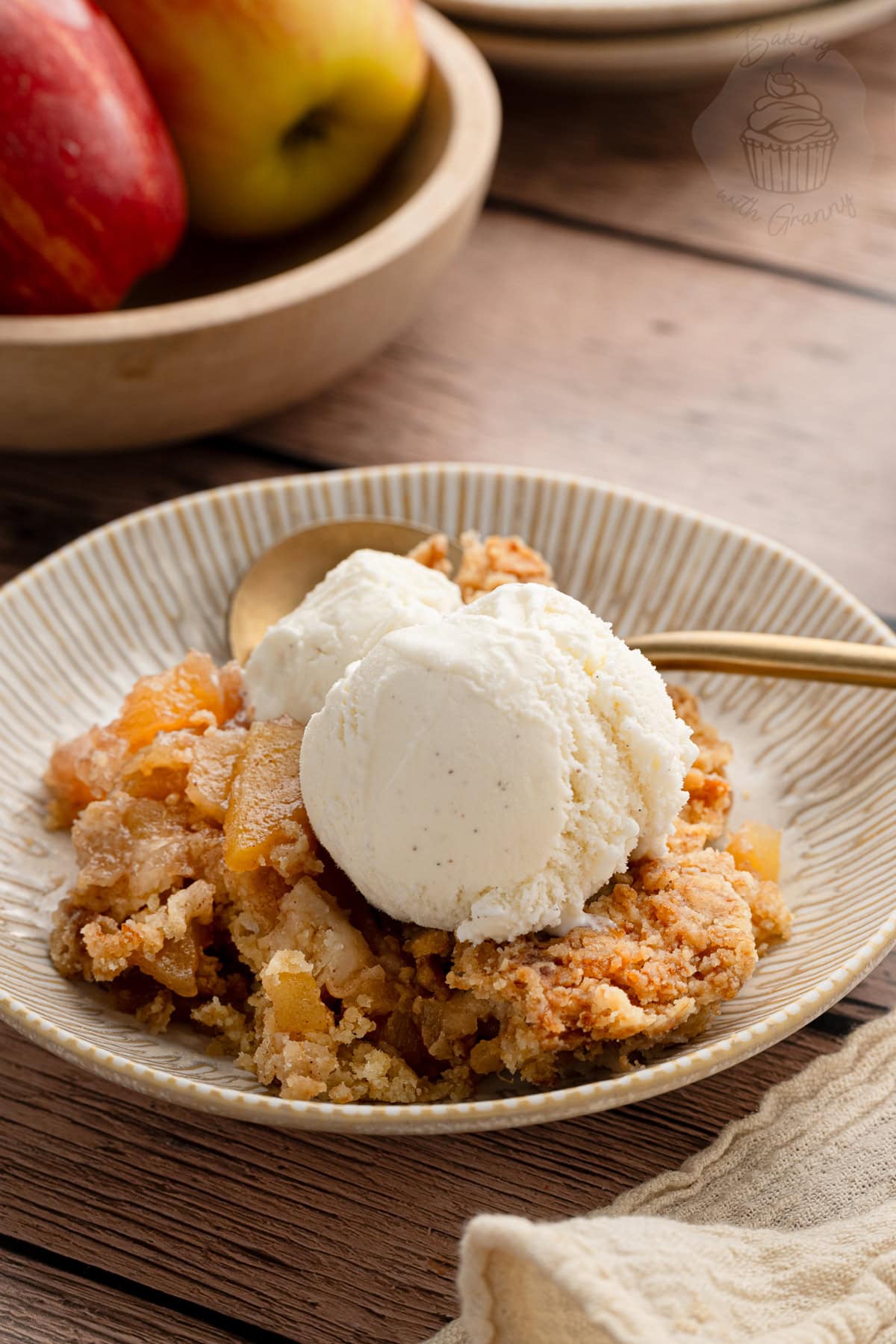Warm apple crumble topped with vanilla ice cream on a ceramic plate.