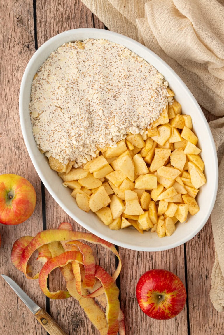 Chopped spiced apples and crumble topping arranged in a white baking dish.