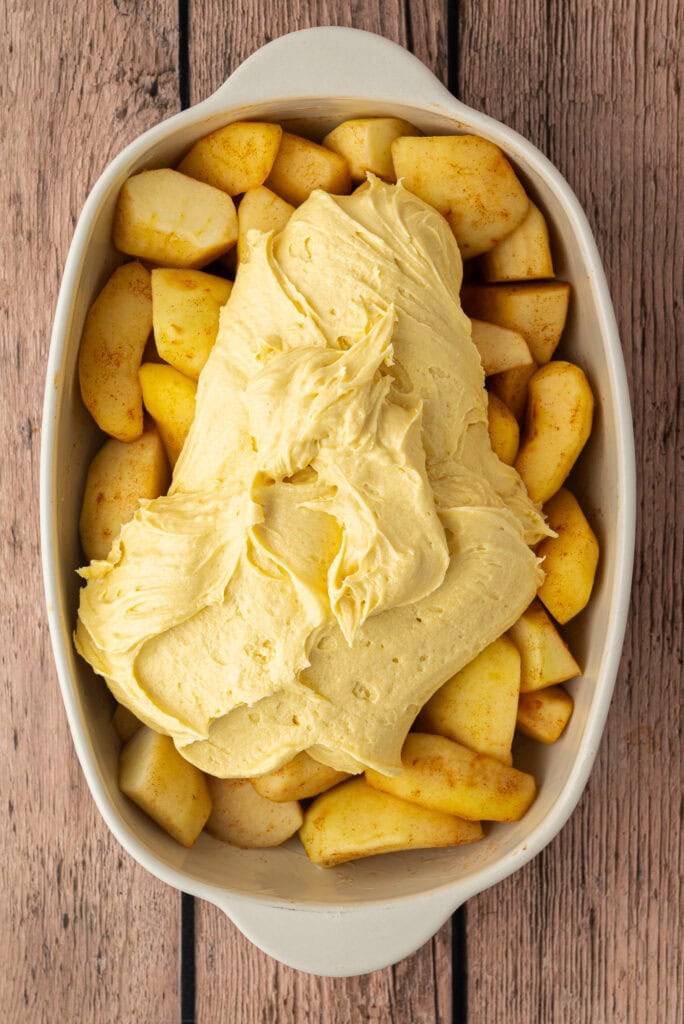 Sponge mixture dolloped over stewed apples in a white baking dish.