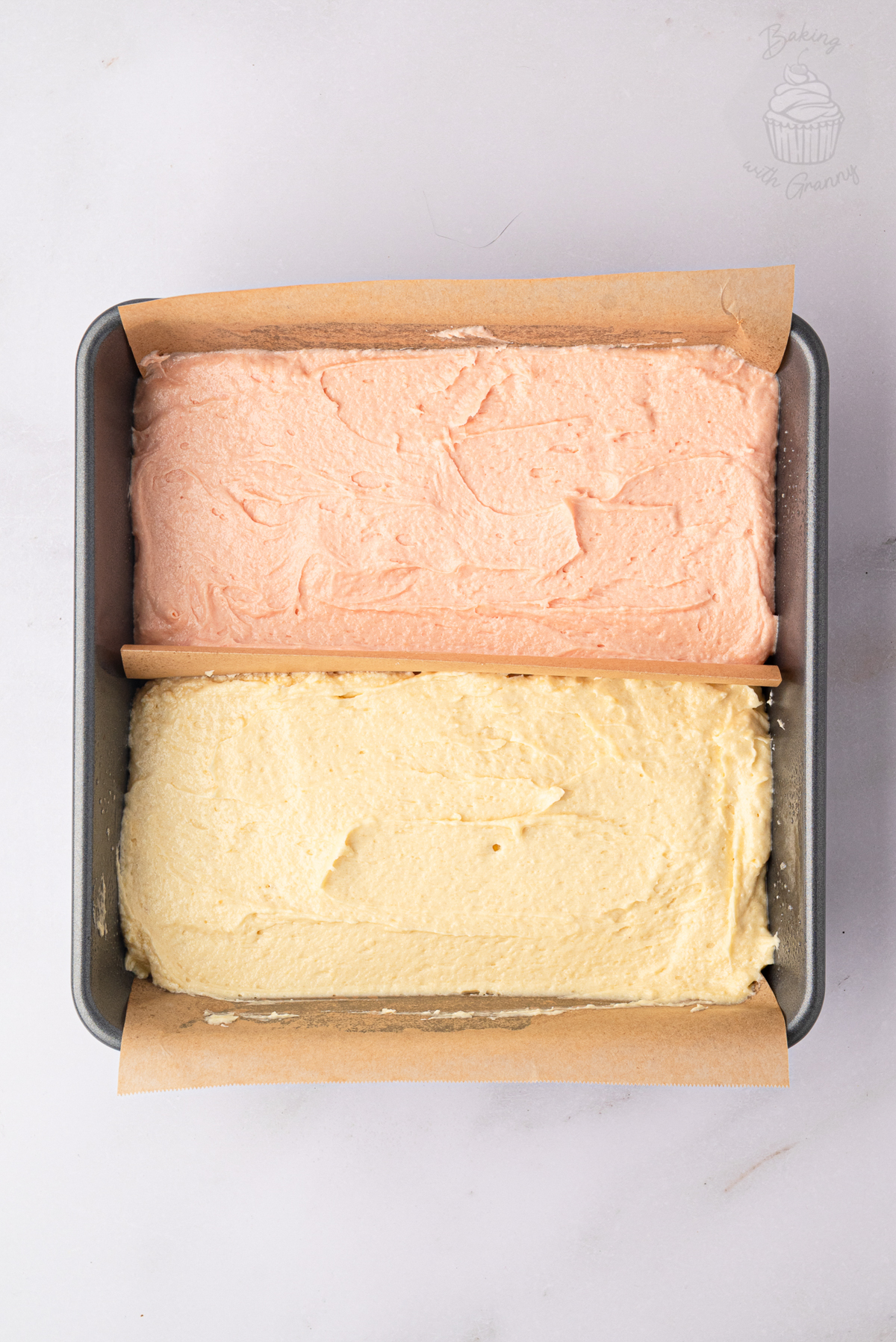 Pink and plain Battenberg cake batter in a divided square cake tin.