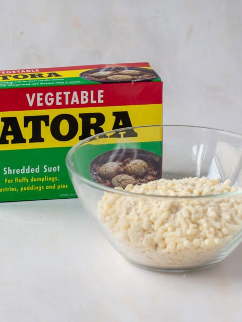 Shredded vegetable suet in a glass bowl beside a box of Atora vegetable suet.