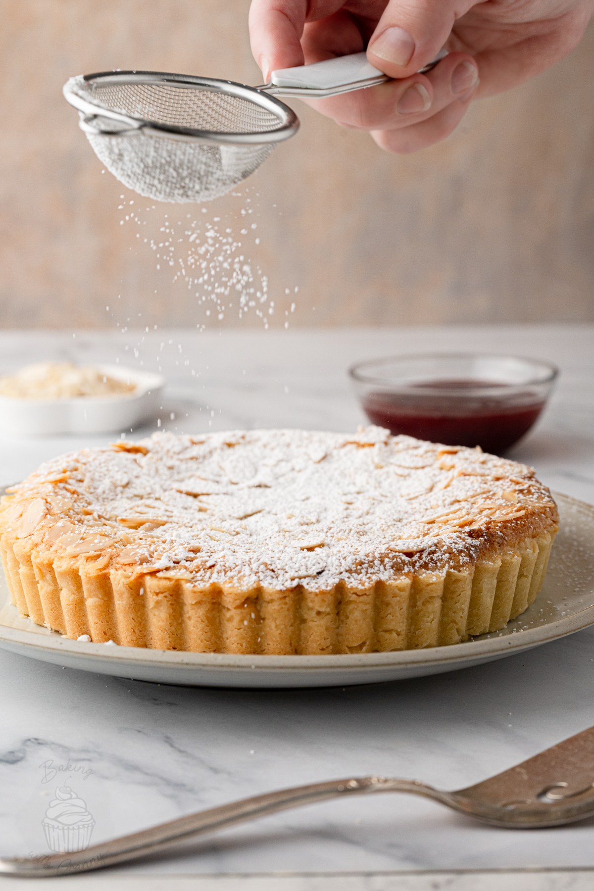 Dusting a Bakewell Tart with icing sugar before serving.