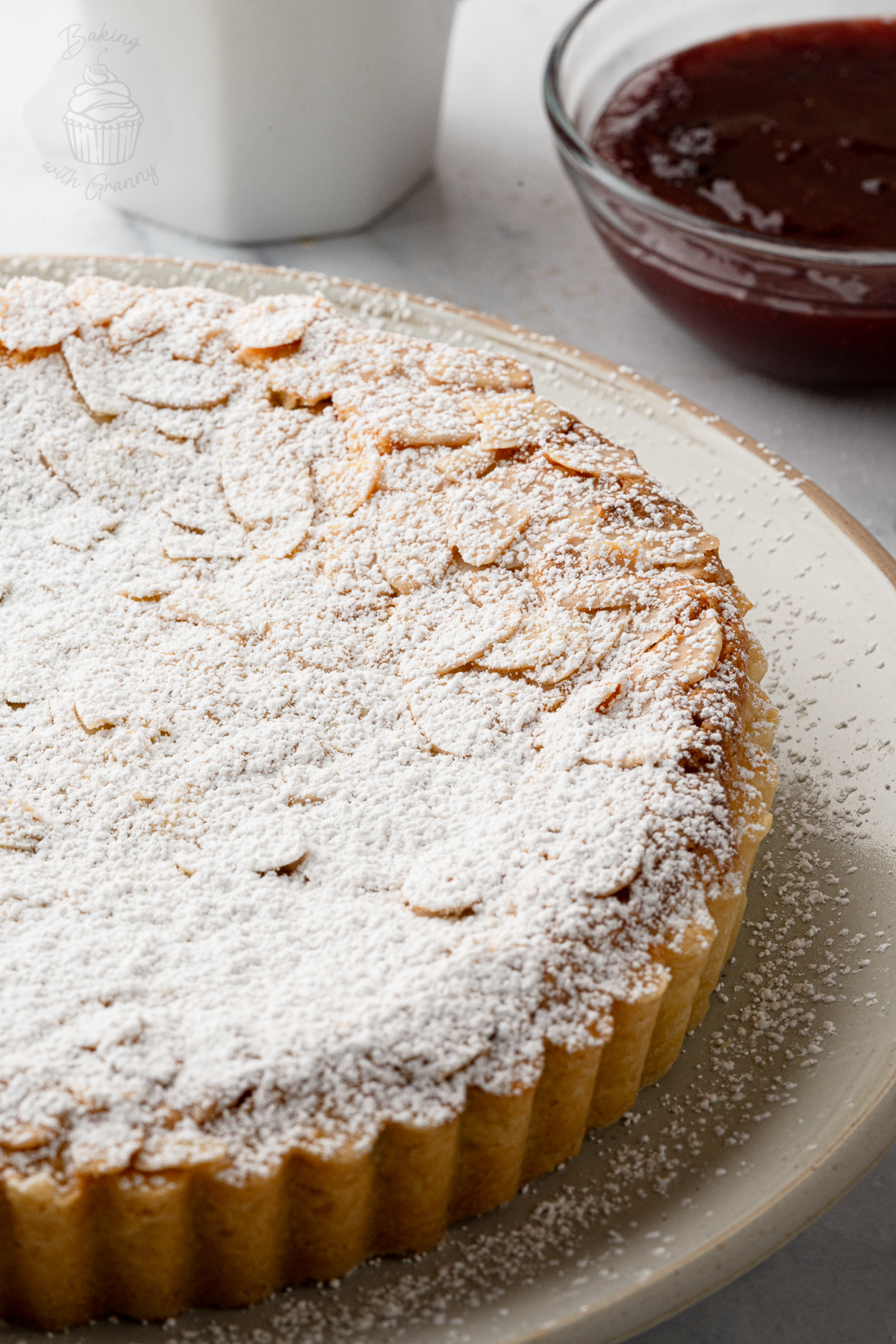 Bakewell Tart dusted with icing sugar beside raspberry jam.