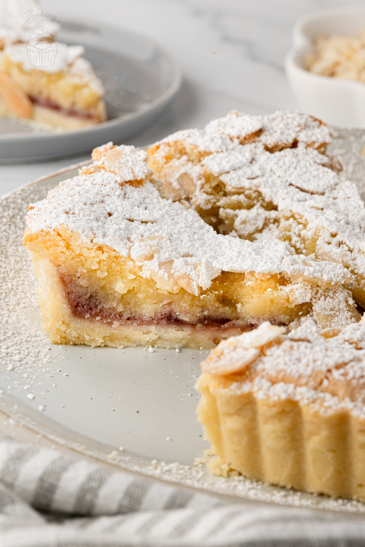 Close-up of a Bakewell Tart slice showing the crisp pastry, raspberry jam and almond filling.