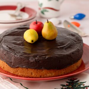 Whole Tunis Cake on a red plate, topped with chocolate ganache and marzipan fruits.