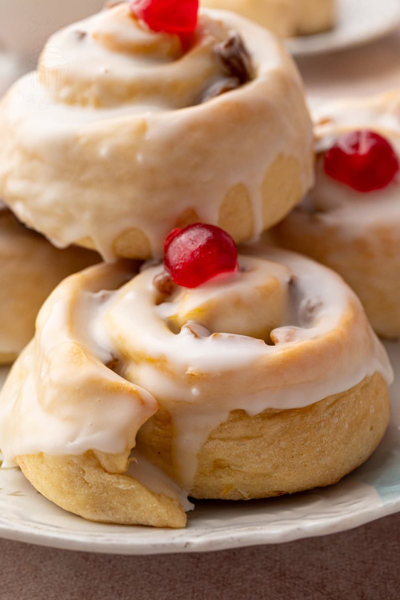 Belgian Buns Side view of stacked Belgian buns on a floral plate, highlighting their soft texture and shiny icing glaze.