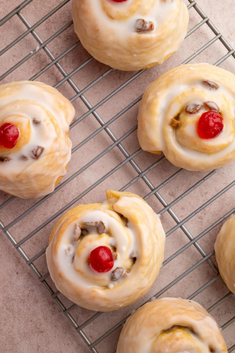 Belgian Buns Overhead view of Belgian buns cooling on a wire rack, all topped with white icing and glacé cherries.
