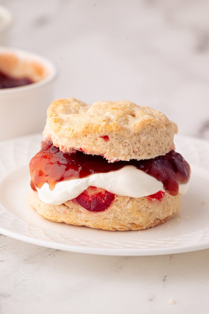 Cherry Scones A cherry scone sandwich on a white plate, filled with fresh cream and strawberry jam. The golden-brown, crumbly scone pairs perfectly with the glossy jam. Its set against a light marble surface, inviting you to enjoy this delightful treat inspired by a beloved cherry scone recipe.