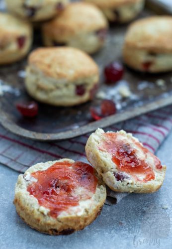 Cherry Scones Cherry scone, cut in half and topped with butter and jam. A tray with more cherry scones lays behind.