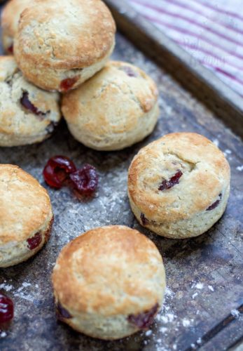 Cherry Scones Overhead photo of a tray of cherry scones on a baking tray; with crumbs, excess flour and glace cherries dotted around them.