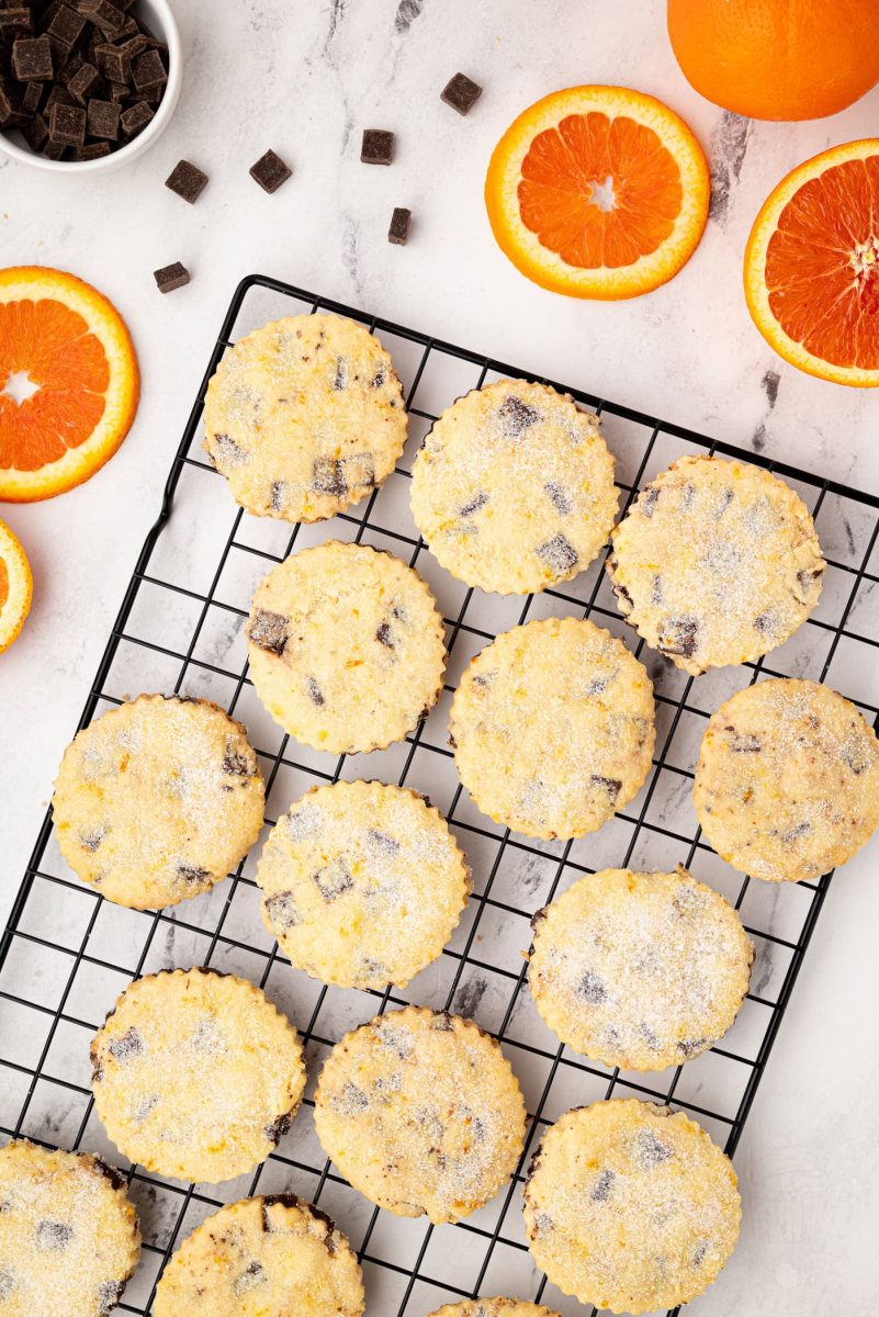 Chocolate Orange Shortbread Overhead view of chocolate orange shortbread cookies on a wire rack, surrounded by orange slices and scattered chocolate chunks.